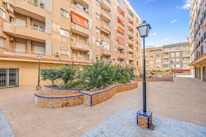 A multi-story residential building with balconies, a tiled courtyard, and a street lamp.