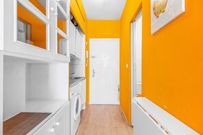 Un couloir étroit avec un lave-linge, une porte et une œuvre d’art accrochée au mur.