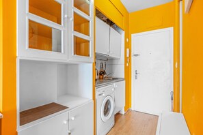 Una cocina compacta con lavadora, armarios blancos y una puerta.
