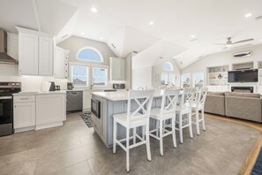 A modern kitchen with white cabinetry, a central island, and a dining area with white chairs.