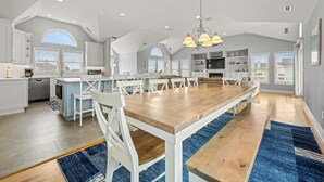 A spacious kitchen with a large wooden table, white chairs, and a blue rug. - A Beach Attitude: Dog-friendly, Private Pool, Hot Tub, 1100 Ft to Beach (Corolla)