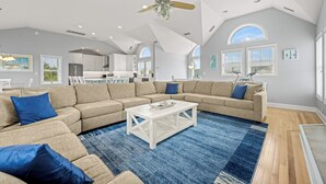 A spacious living room with a large sectional sofa, a white coffee table, and a blue area rug. - A Beach Attitude: Dog-friendly, Private Pool, Hot Tub, 1100 Ft to Beach (Corolla)