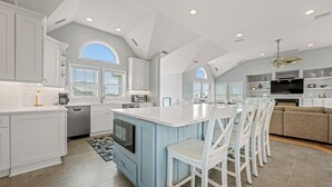 A spacious kitchen with white cabinetry, a blue island, and a dining area with white chairs. - A Beach Attitude: Dog-friendly, Private Pool, Hot Tub, 1100 Ft to Beach (Corolla)