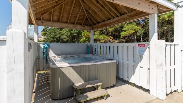A hot tub under a wooden pergola with a white fence and a caution sign. - A Beach Attitude: Dog-friendly, Private Pool, Hot Tub, 1100 Ft to Beach (Corolla)