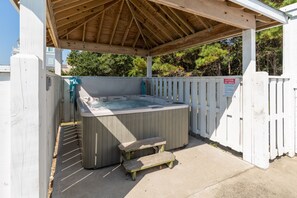 Un jacuzzi bajo una pérgola de madera, con una cerca blanca y un letrero de precaución.