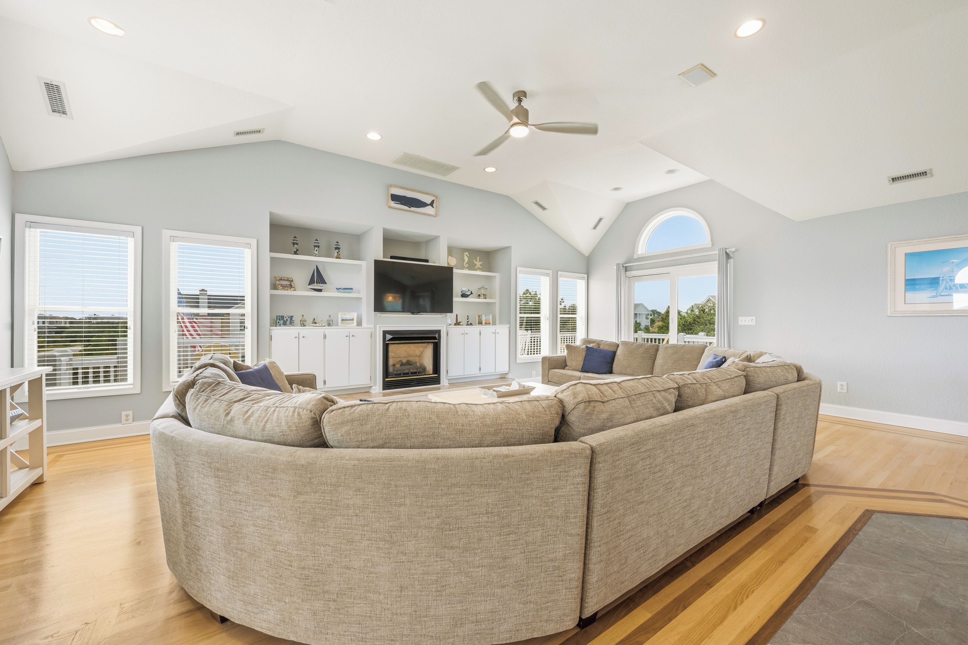 A spacious living room with a large L-shaped sectional sofa, a fireplace, and a ceiling fan.