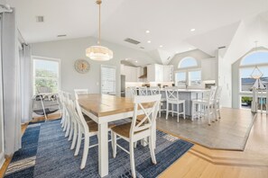 A spacious kitchen with white cabinetry, a central island, and a dining area with a wooden table and white chairs.
