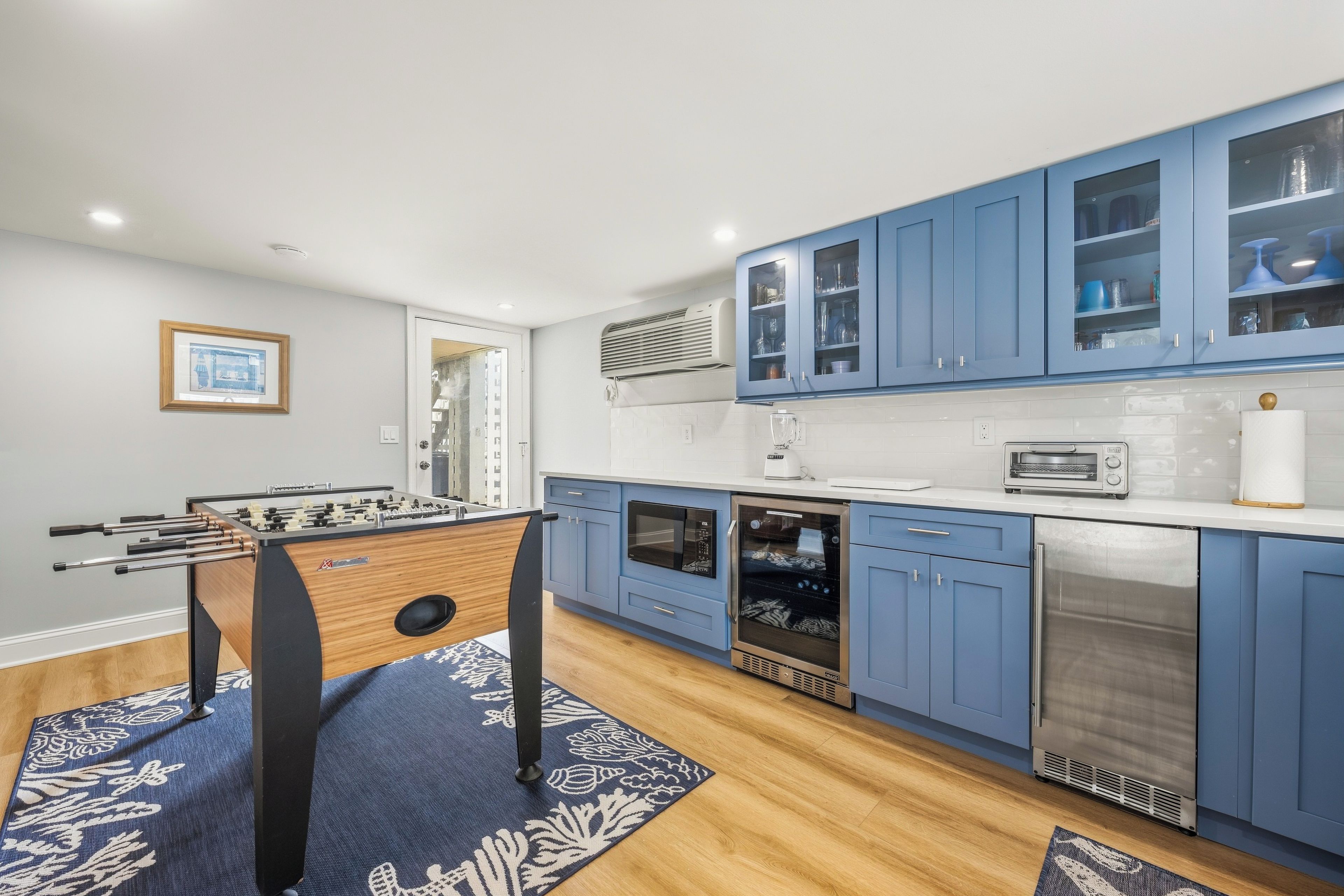 A modern kitchen with blue cabinets, a foosball table, a microwave, and a dishwasher.