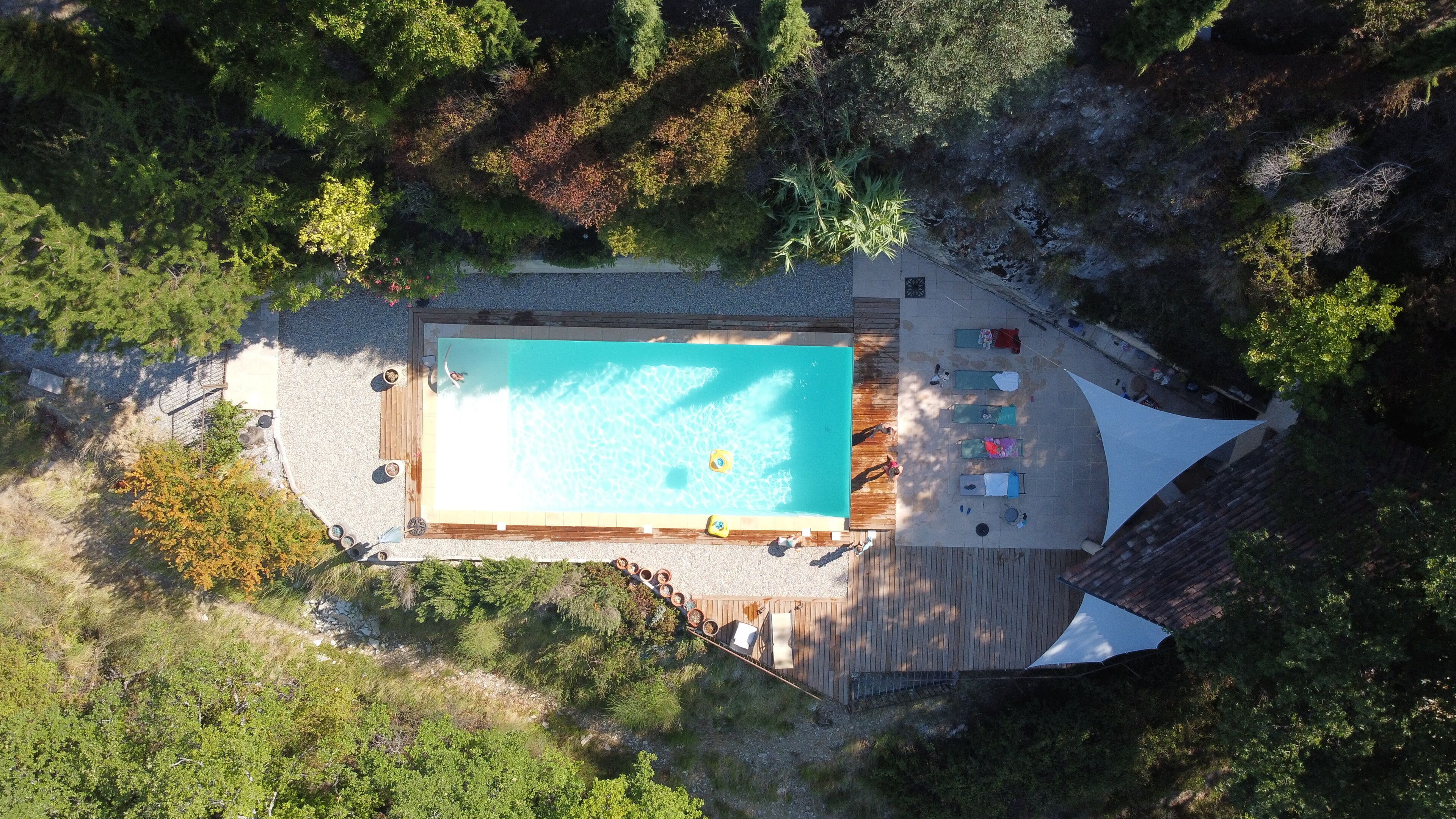 An aerial view of a rectangular swimming pool surrounded by a deck with lounge chairs and a shaded area.