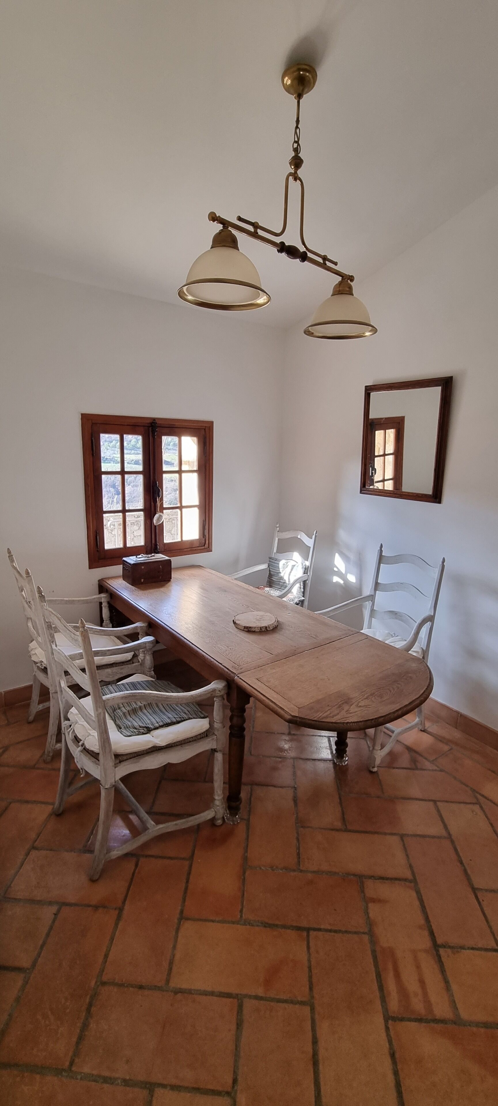 A dining area with a wooden table, white chairs, a chandelier, and a window with a view.