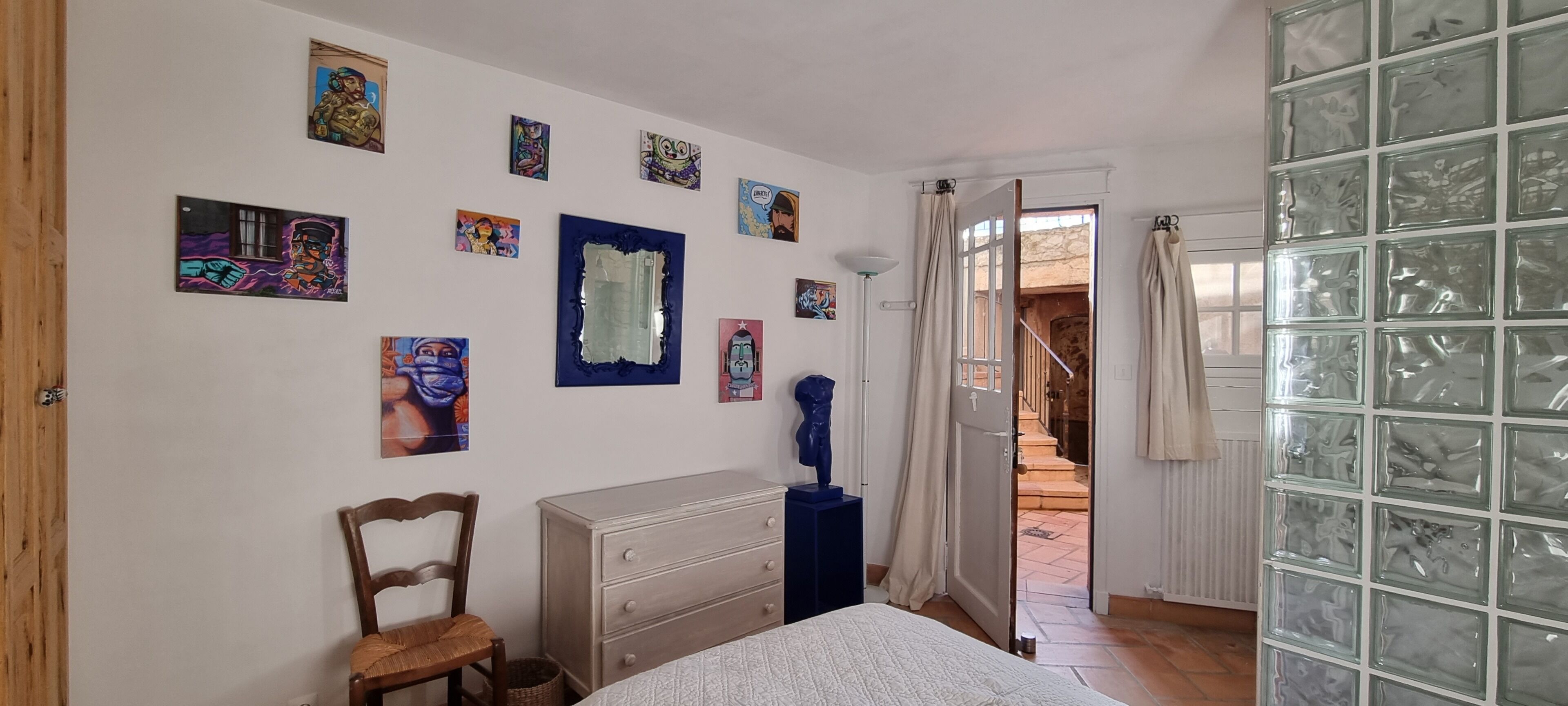 Une chambre à coucher comprenant un lit, une commode, une chaise et diverses œuvres d’art murales.