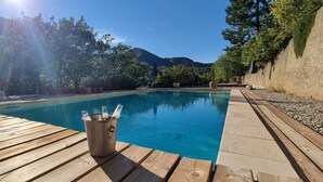 A wooden deck with a pool, surrounded by trees and mountains. - Beautiful provencal house with a view, hanging gardens & a great swimming pool  (Montaulieu)
