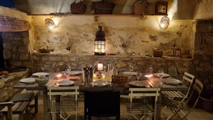 A rustic stone interior with a long dining table set for a meal, surrounded by stone walls and wooden furniture. - Beautiful provencal house with a view, hanging gardens & a great swimming pool  (Montaulieu)