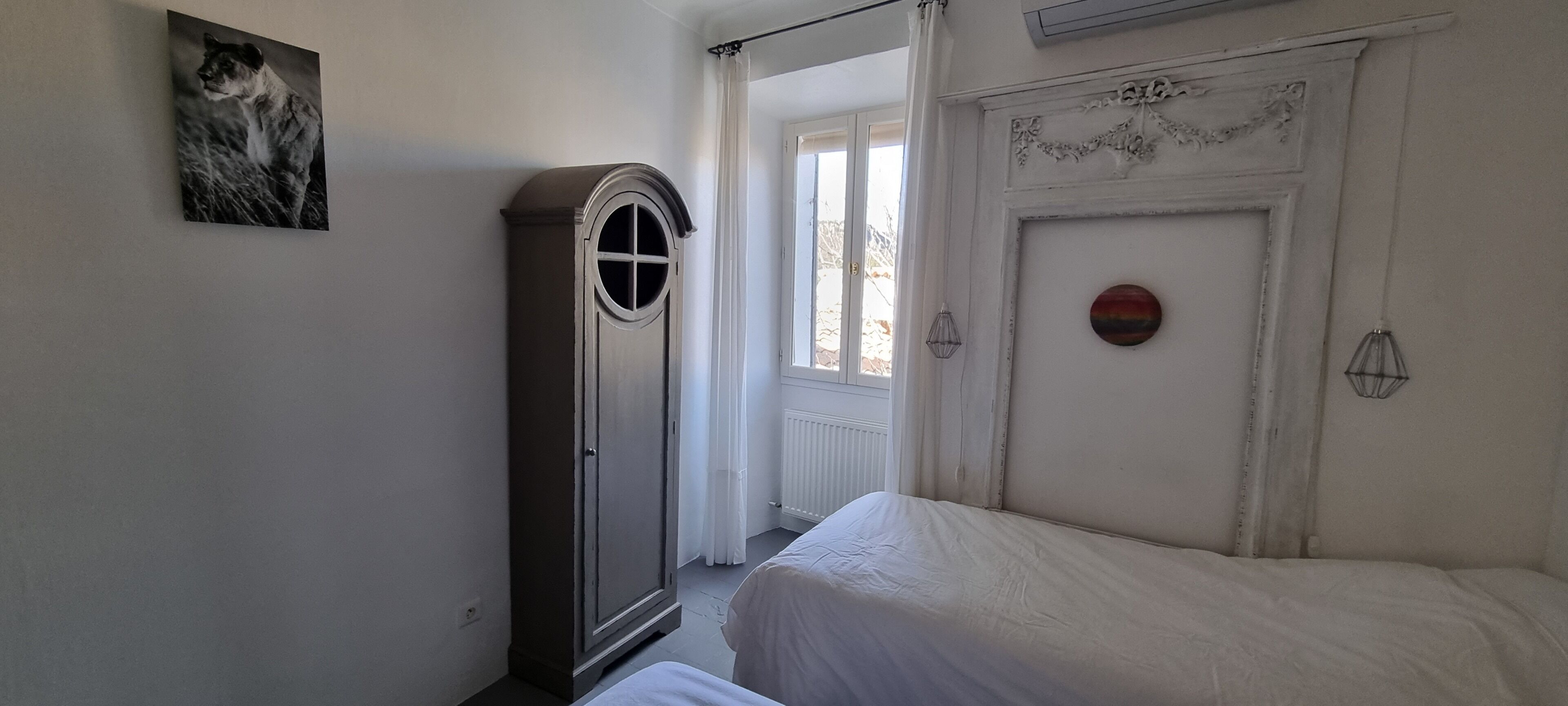 Un dormitorio con cama, armario, puerta con panel decorativo y ventana con cortinas.