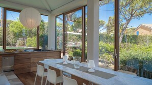 A modern kitchen with a marble countertop, white chairs, and a large window overlooking a garden.
