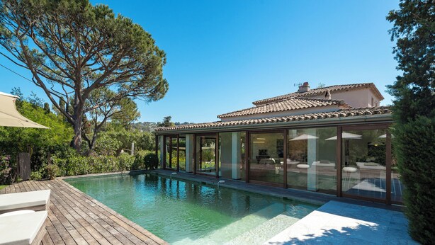 A modern house with a swimming pool, wooden deck, and large glass windows.