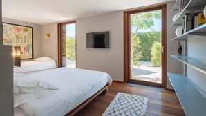 A bedroom with a bed, a TV, a bookshelf, and a large window with a view of greenery.