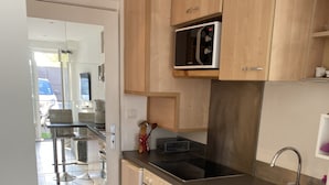 A modern kitchen with wooden cabinets, a stainless steel sink, and a built-in oven. - Studio Avec Petit Déjeuner (Le Rouret)