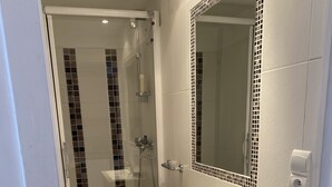 A modern bathroom with a glass-enclosed shower, a white sink, and a mirror with a decorative border. - Studio Avec Petit Déjeuner (Le Rouret)