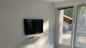 A modern living room with a flat-screen TV mounted on the wall, a grey sofa, and a bench. - Studio Avec Petit Déjeuner (Le Rouret)