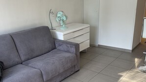 A modern living room with a grey sofa, a white dresser, and a small teal fan. - Studio Avec Petit Déjeuner (Le Rouret)