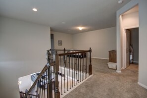 A spacious hallway with a carpeted floor, a wooden staircase with a railing, and a door leading to another room. - Affordable 3-Bedroom Townhouse With Backyard ~ Double Story (Pet Friendly!) (Rosenberg)