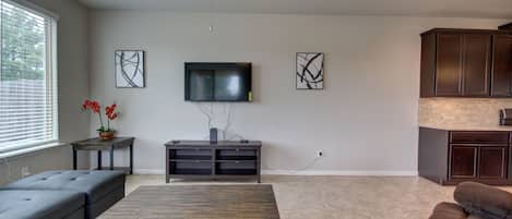 Een ruime woonkamer met een grote houten tafel, een bank, een aan de muur bevestigde televisie en een plafondventilator.