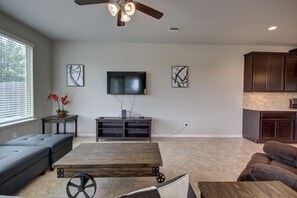 A spacious living room with a large wooden table, a sofa, a television mounted on the wall, and a ceiling fan. - Affordable 3-Bedroom Townhouse With Backyard ~ Double Story (Pet Friendly!) (Rosenberg)