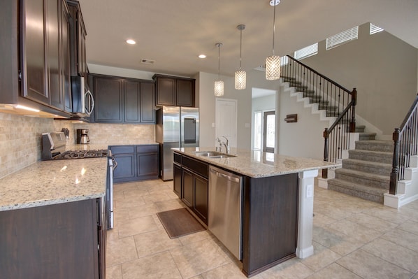 A modern kitchen with dark cabinets, stainless steel appliances, and a central island. - Affordable 3-Bedroom Townhouse With Backyard ~ Double Story (Pet Friendly!) (Rosenberg)