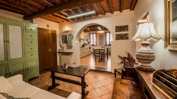 Una sala de estar acogedora con techo de madera, un armario verde, una zona de comedor con mesa y sillas, y una cocina visible a través de un arco.