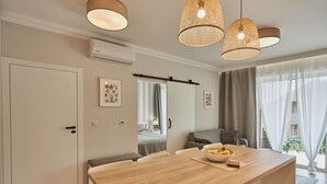 A modern kitchen with a wooden countertop, hanging pendant lights, and a view of the living area.