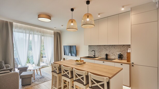 A modern kitchen with a wooden island, pendant lights, and a large window with curtains.