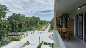 A balcony with a view of a landscaped area, a wooden table, and a modern building with glass doors.