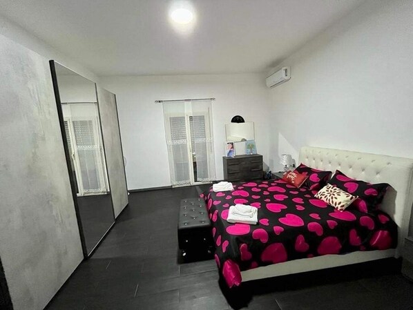 A bedroom with a bed, a nightstand, a mirror, and a door.