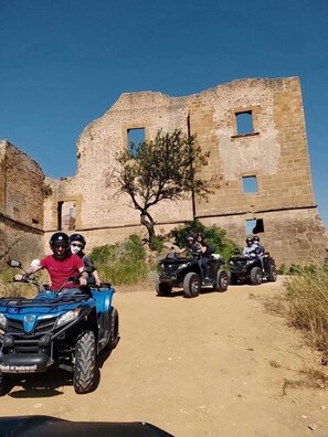 A group of people on ATVs in front of a stone building with a tree in the center.