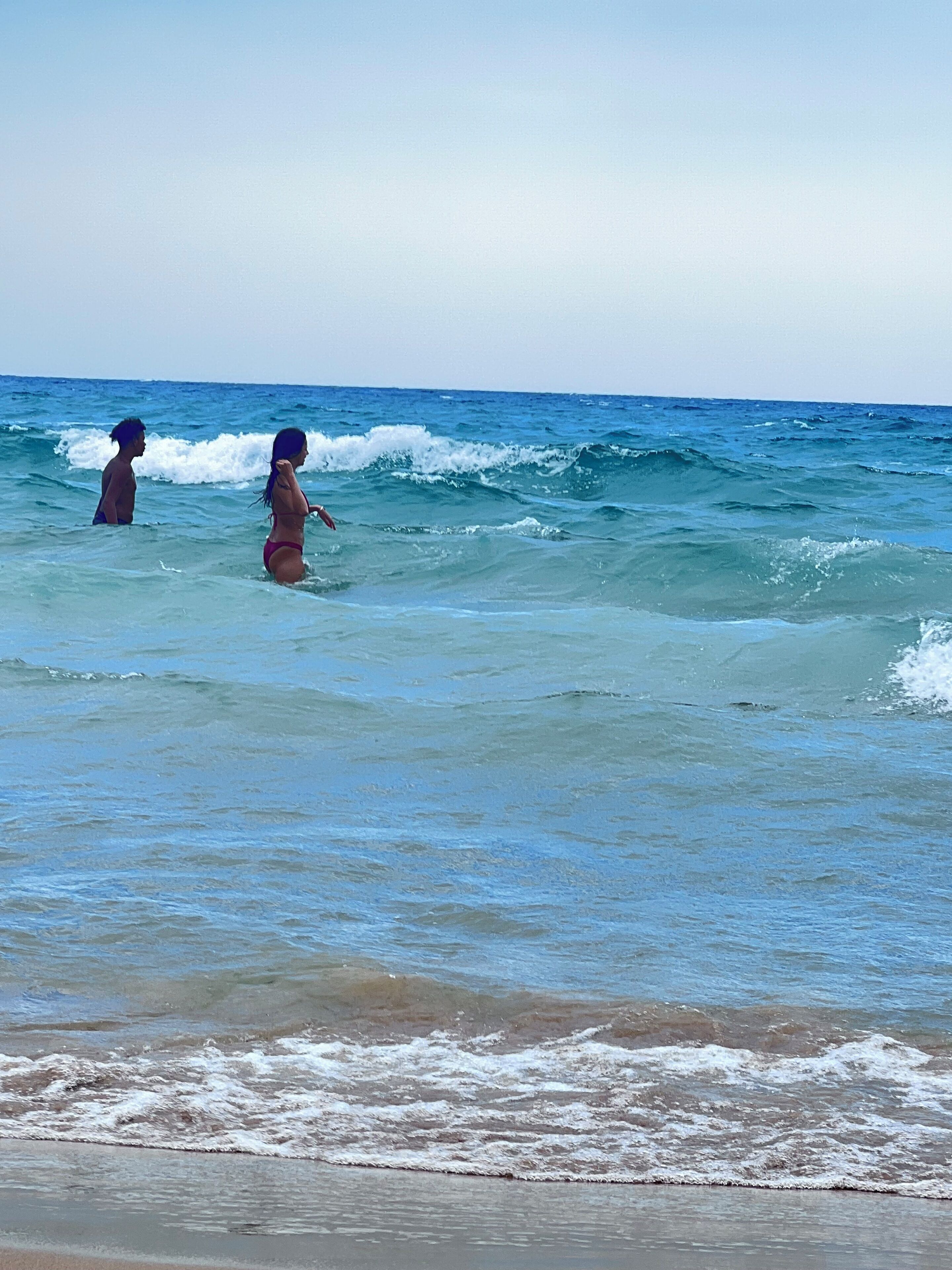 A beach with waves and two people in the water.