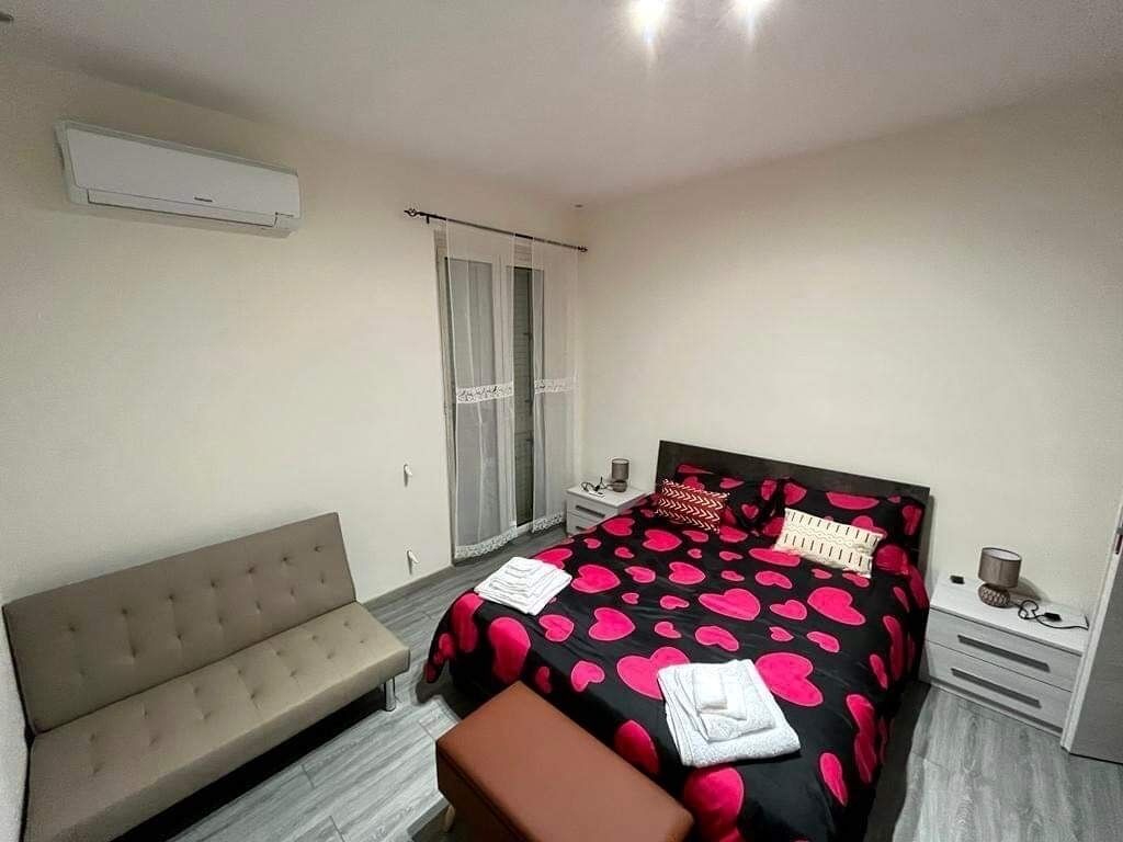 A bedroom with a bed, a bench, a nightstand, and a window with curtains.