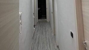 A narrow hallway with a wooden door on the right and a white door on the left, leading to a dark room. - KAM DELUXE 120 sqm bright suitable Groups,Families,Couples,Singles<br><br> (Calamonaci)
