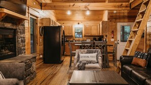 L’intérieur chaleureux d’un chalet avec une cheminée en pierre, un plafond en bois, un coin repas et un salon comprenant un canapé et une table basse.