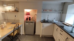 A compact kitchen with a refrigerator, sink, and a dining area with a table and chairs. - Bijoux Cottage in Porthleven  5 mins walk  Beach/Harbour. Sleeps 2. Dog Friendly (Porthleven)