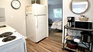 A compact kitchen with a white refrigerator, stove, and microwave. A small dining area is visible through an open door.