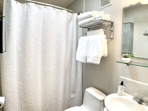 A bathroom with a shower curtain, a toilet, a sink, a towel rack, and a small plant on a glass shelf. - Beach & Redwoods 5mins from Unexpected Oasis (Crescent City)