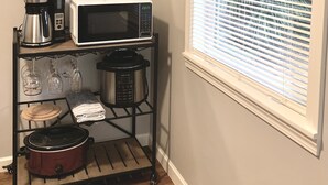 A kitchen with a microwave, coffee maker, and a slow cooker on a rack. There is a window with blinds and a mirror on the wall.