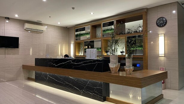 A modern reception desk with a marble top, wooden paneling, and a digital clock.