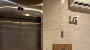 A modern elevator with a digital display, a wooden panel, and a Samsung air conditioning unit.