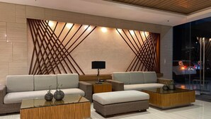 A modern living room with a sofa set, two coffee tables, and a wall with a geometric pattern.
