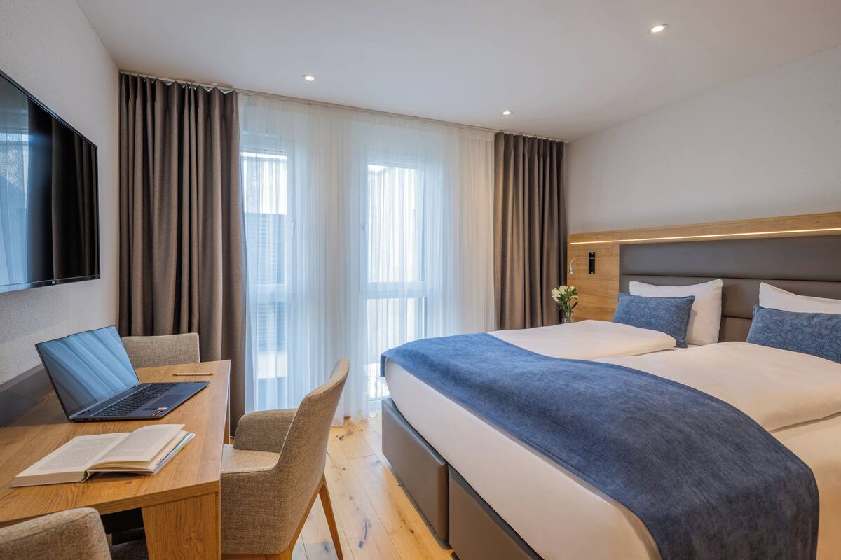 Een hotelkamer met een bed, een bureau met een laptop, een stoel en een televisie.
