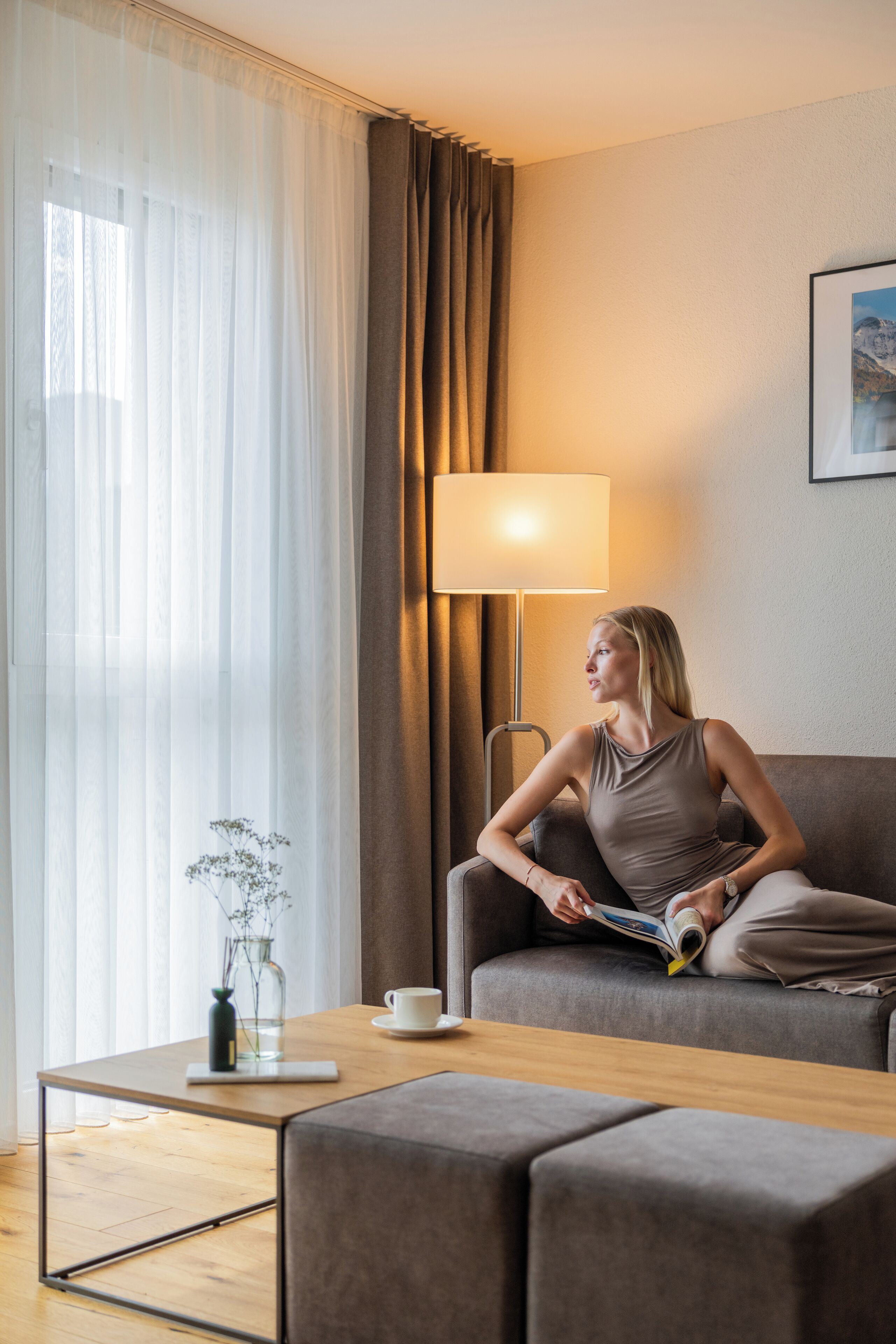A modern living room with a sofa, a coffee table, a lamp, and a vase with flowers.