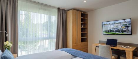 A hotel room with a large bed, a desk with a laptop, a television on the wall, and a window with curtains.