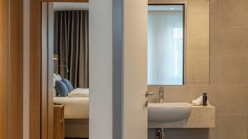 Une chambre d’hôtel moderne, avec un lit, une salle de bain dotée d’un lavabo et d’un miroir, et une vue sur la pièce depuis l’entrée.